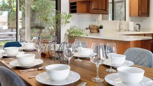 A dining table set with white bowls, plates, and cutlery, accompanied by wine glasses, in a room with wooden cabinets and a view of the outdoors. - Spacious 3BR/2BA Central Sac – Fireside Comfort (Sacramento)