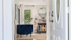 A hallway with a fireplace, a round mirror, and a dark blue chair. - Spacious 3BR/2BA Central Sac – Fireside Comfort (Sacramento)