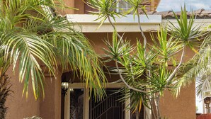 A house with a concrete pathway leading to a gated entrance, surrounded by various tropical plants. - Perfect Family Home w/ Private Outdoor Space! (San Diego)