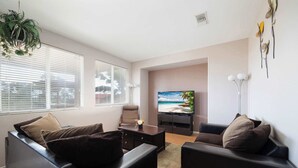 A modern living room with a sofa, a coffee table, and a TV displaying a beach scene. - Perfect Family Home w/ Private Outdoor Space! (San Diego)