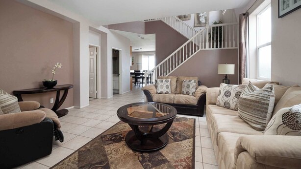 A spacious living room with a beige sofa set, a glass coffee table, and a staircase leading to an upper floor. - Perfect Family Home w/ Private Outdoor Space! (San Diego)