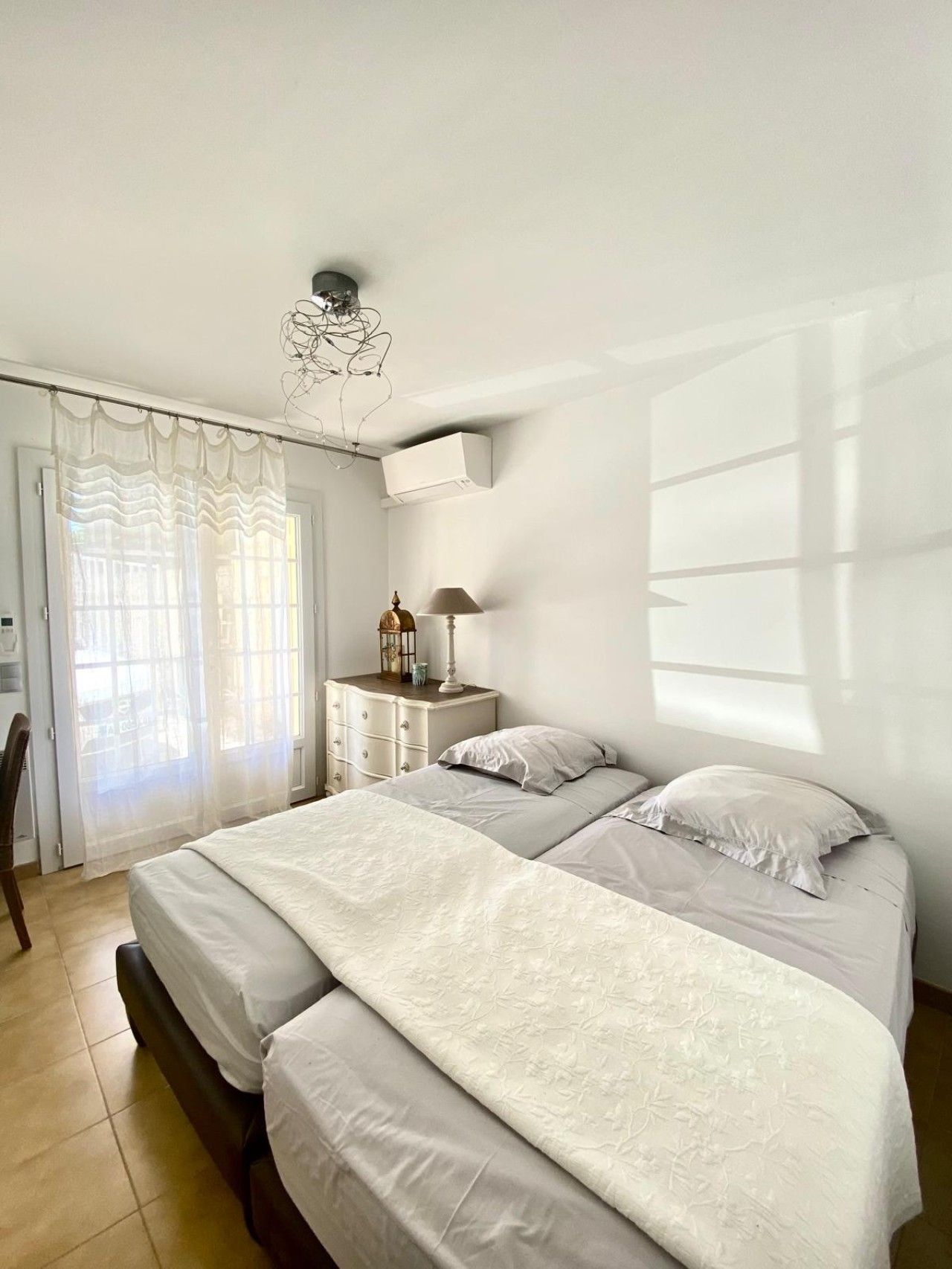 A bedroom with two beds, a dresser, a lamp, and a ceiling light fixture.