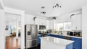 A modern kitchen with white and blue cabinets, stainless steel appliances, and a central island. - Grand 6BR 3BA Pool Escape Round Rock (Round Rock)
