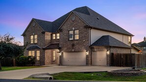 A two-story house with a brick facade, two garage doors, and a well-maintained lawn. - Grand 6BR 3BA Pool Escape Round Rock (Round Rock)