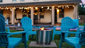 A patio area with a fire pit surrounded by blue chairs, a house in the background, and string lights overhead. - Grand 6BR 3BA Pool Escape Round Rock (Round Rock)