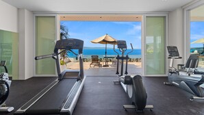 Een sportschool met loopbanden, elliptische trainers en uitzicht op de oceaan door grote ramen.