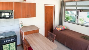 A compact kitchen with wooden cabinets, a built-in stove, and a dining table with chairs. - Fare Kale (Moorea-Maiao)
