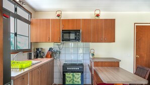 A compact kitchen with wooden cabinets, a microwave, a stove, and a small dining table with chairs. - Fare Kale (Moorea-Maiao)