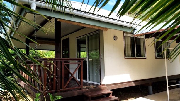 A two-story house with a porch, wooden steps, and a glass door leading to a covered area. - Fare Kale (Moorea-Maiao)