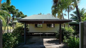 A single-story building with a corrugated metal roof, surrounded by lush greenery and palm trees. - Fare Kale (Moorea-Maiao)