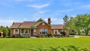 A two-story brick house with a front porch, a chimney, and a well-maintained lawn. - Modern country house w/firepit. (Alma)