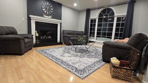 A living room with a fireplace, two armchairs, a coffee table, and a large window. - Modern country house w/firepit. (Alma)