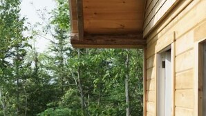 A wooden deck with a barbecue grill, surrounded by a wooden railing and a door leading to a covered area. - Les Cabines St-O - 2 (St-Onésime d'Ixworth)