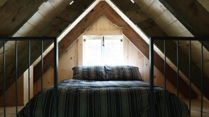 A bedroom with a sloped ceiling, a bed with striped bedding, and a window at the end of the room. - Les Cabines St-O - 2 (St-Onésime d'Ixworth)