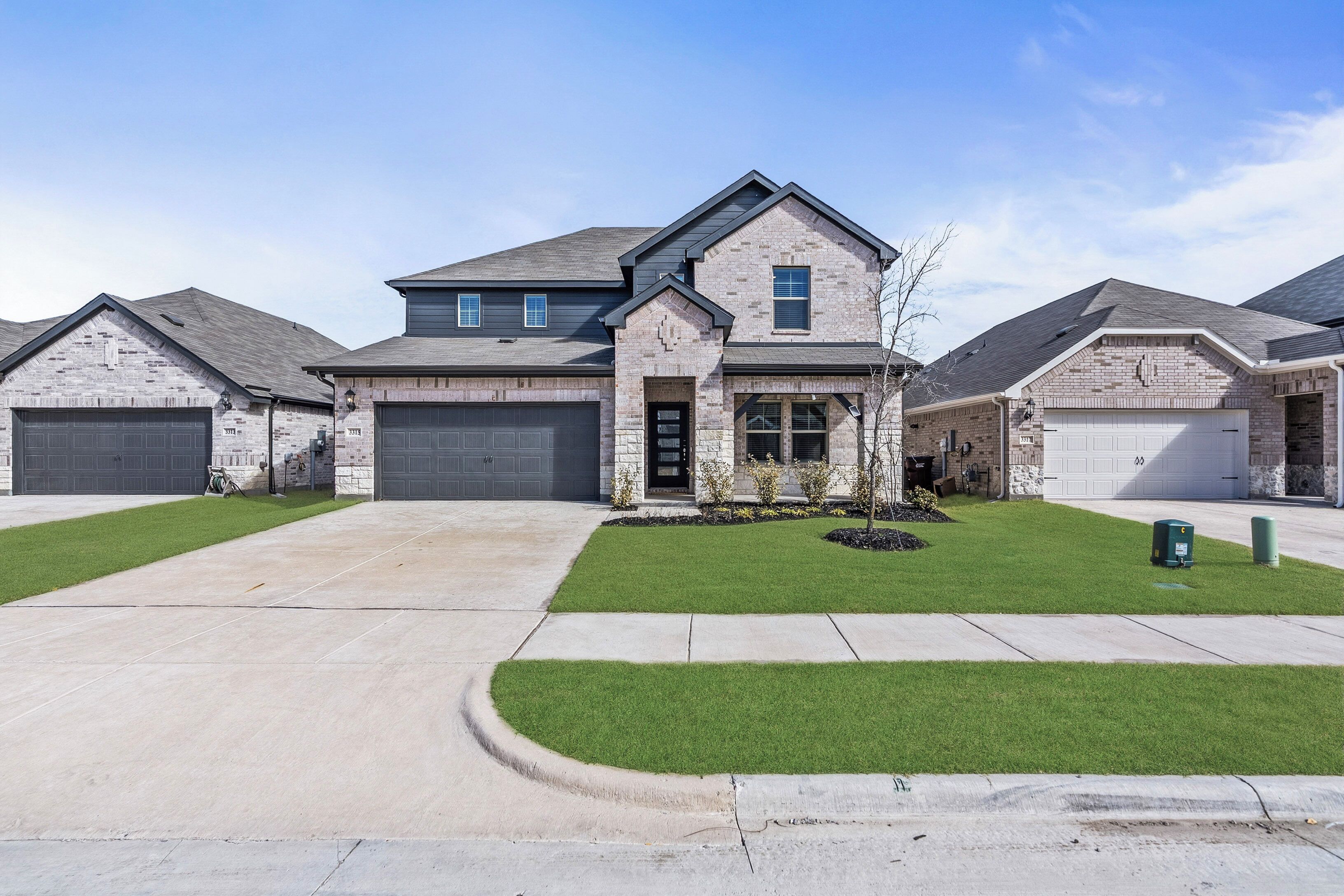 A residential building with a stone facade, two garage doors, and a well-maintained lawn.