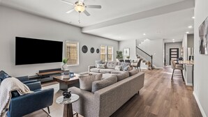 Uma sala de estar moderna com televisão de tela plana, sofás cinzas, uma mesa de centro e um ventilador de teto.