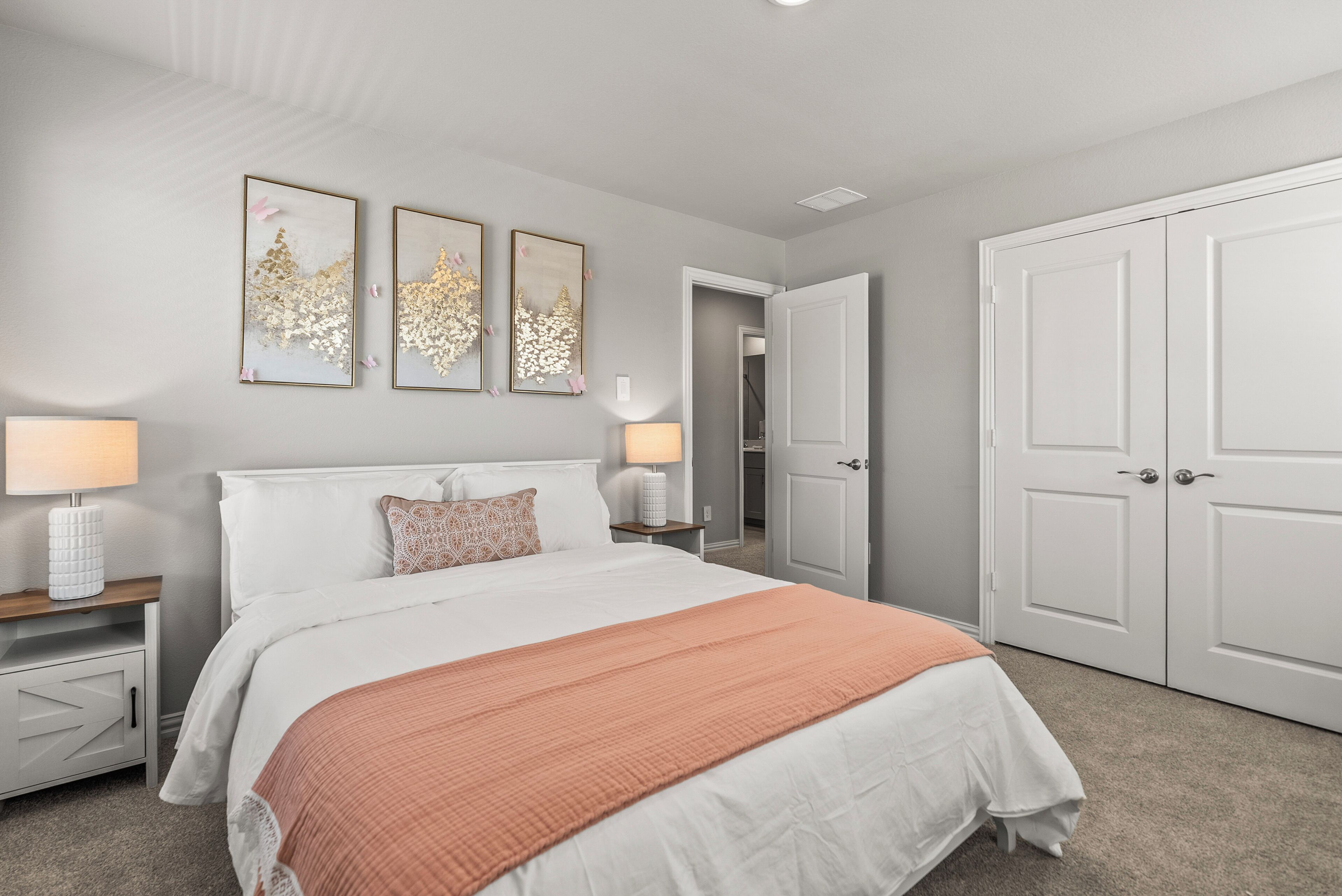 A bedroom with a bed, two bedside tables, a nightstand, a door, and a wall with three framed pictures.