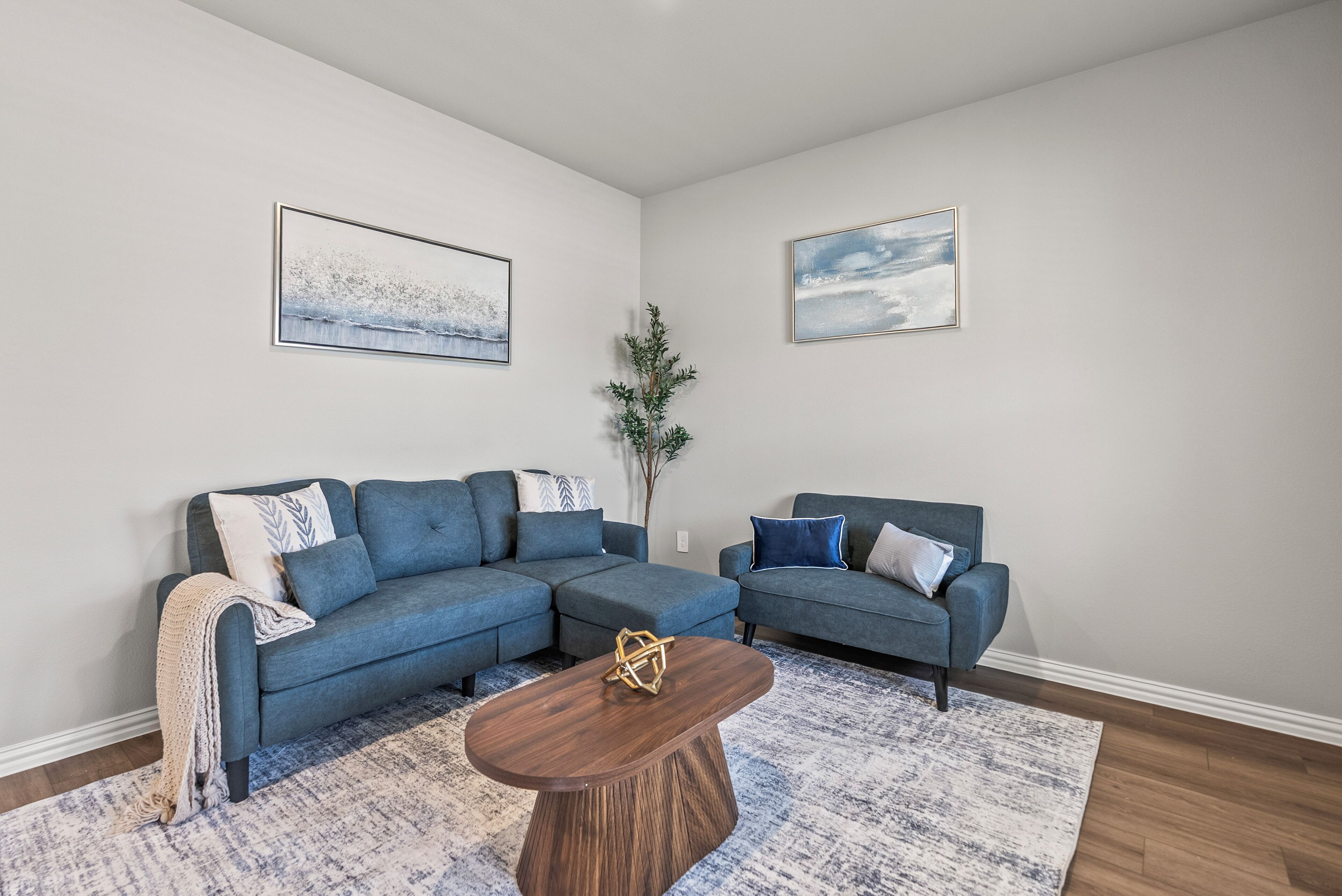 A living room with two blue sofas, a wooden coffee table, and two framed pictures on the walls.