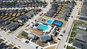 Vista aérea de um bairro residencial com várias casas, uma piscina, quadras de tênis e um estacionamento.