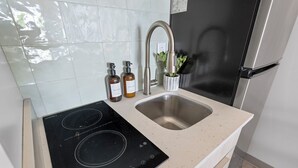 A kitchen with a black induction cooktop, a stainless steel sink, and two soap dispensers. - Studio | near Aquarium, Coolridge Park (Chattanooga)