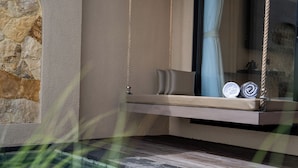 A modern room with a stone accent wall, a hanging swing seat with cushions, and a view of a pool. - Mount Valley Inn Kintamani (Kintamani)