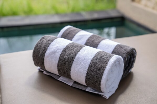 A pair of striped towels on a beige chair by a pool. - Mount Valley Inn Kintamani (Kintamani)