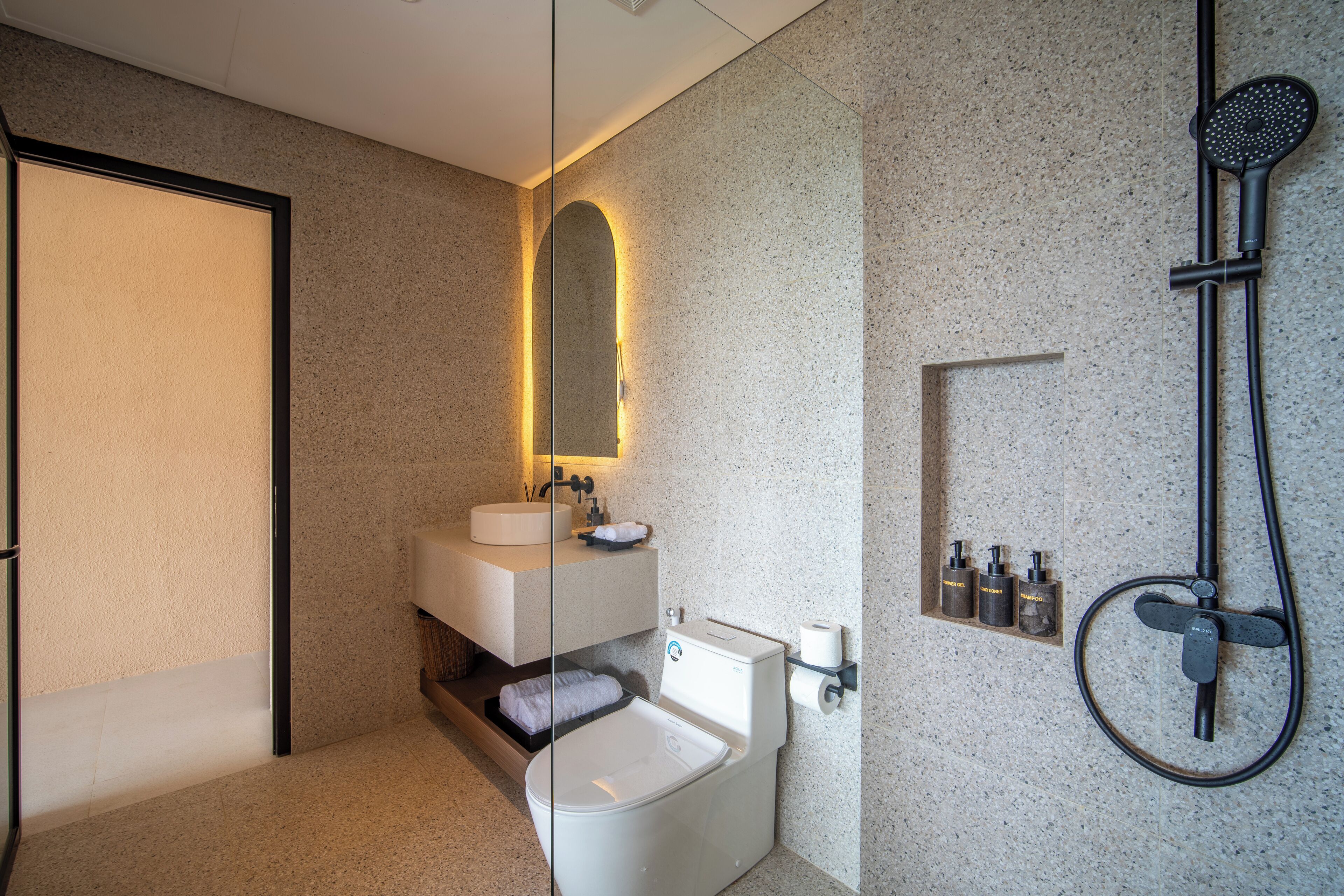 Une salle de bain moderne avec des toilettes sur pied, un lavabo avec un miroir et une douche équipée d’un pommeau de douche à main.
