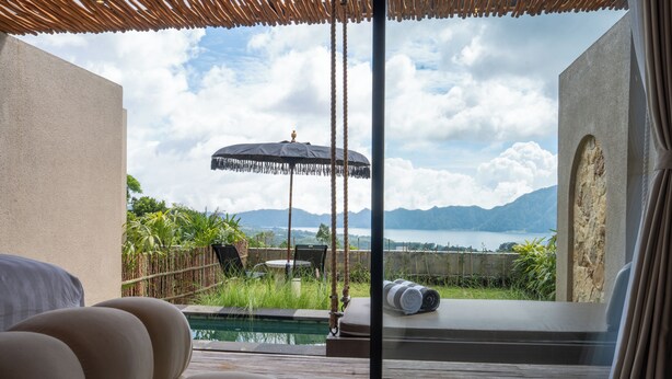 A room with a view of a pool and mountains. There are chairs and an umbrella outside. - Mount Valley Inn Kintamani (Kintamani)