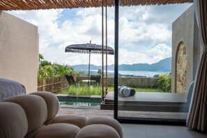 A room with a view of a pool and mountains. There are chairs and an umbrella outside. - Mount Valley Inn Kintamani (Kintamani)