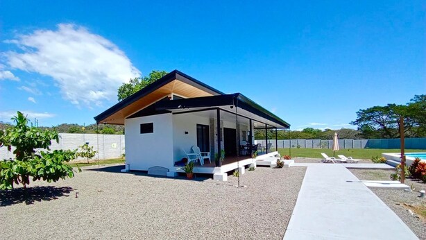 A modern house with a covered patio, a gravel driveway, and a pool in the background. - Quinta Los Monos : Private Swimming Pool : Pet-friendly (Paquera)