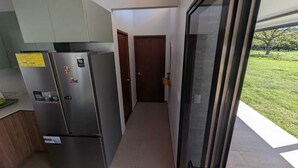 A modern kitchen with a stainless steel refrigerator, a wooden cabinet, and a glass door leading to a balcony with a grassy view. - Quinta Los Monos : Private Swimming Pool : Pet-friendly (Paquera)