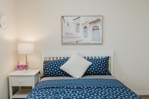 A bedroom with a bed, a bedside table with a lamp, a framed picture on the wall, and a nightstand with a tissue box.
