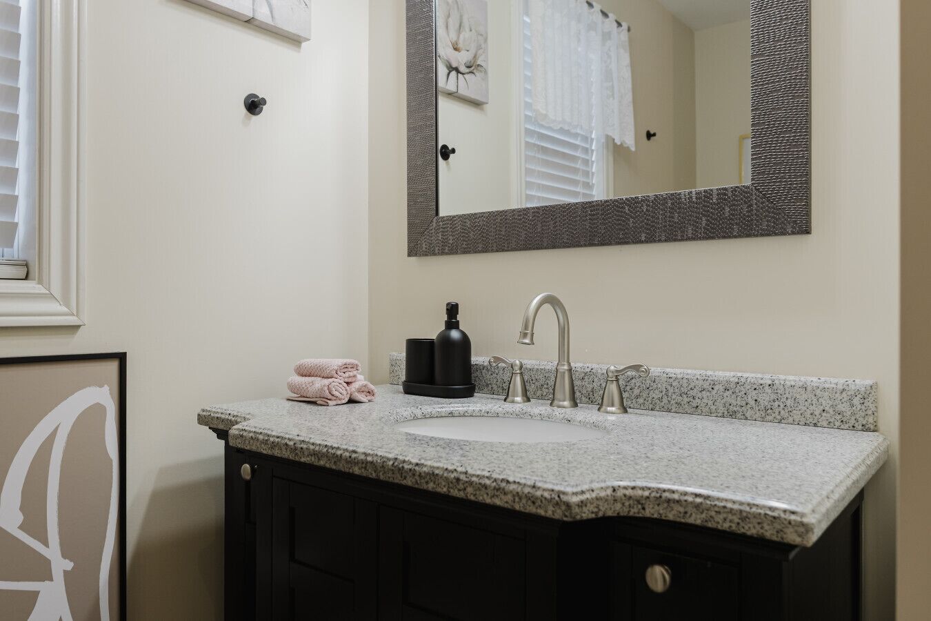 Un baño con encimera de granito, un lavabo, un espejo y un perchero para toallas.
