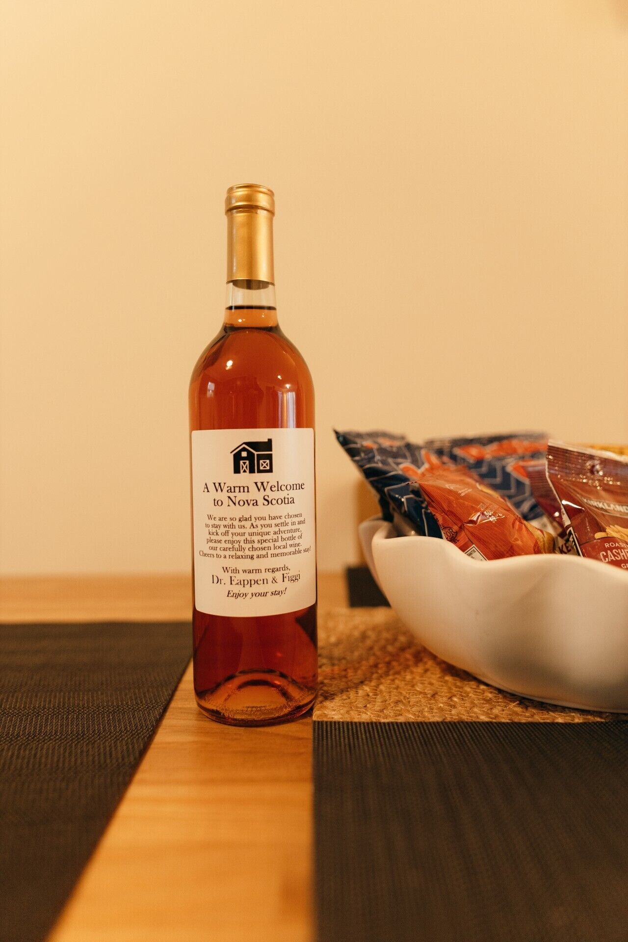 Une bouteille de vin avec une étiquette, un bol de collations et une table en bois.