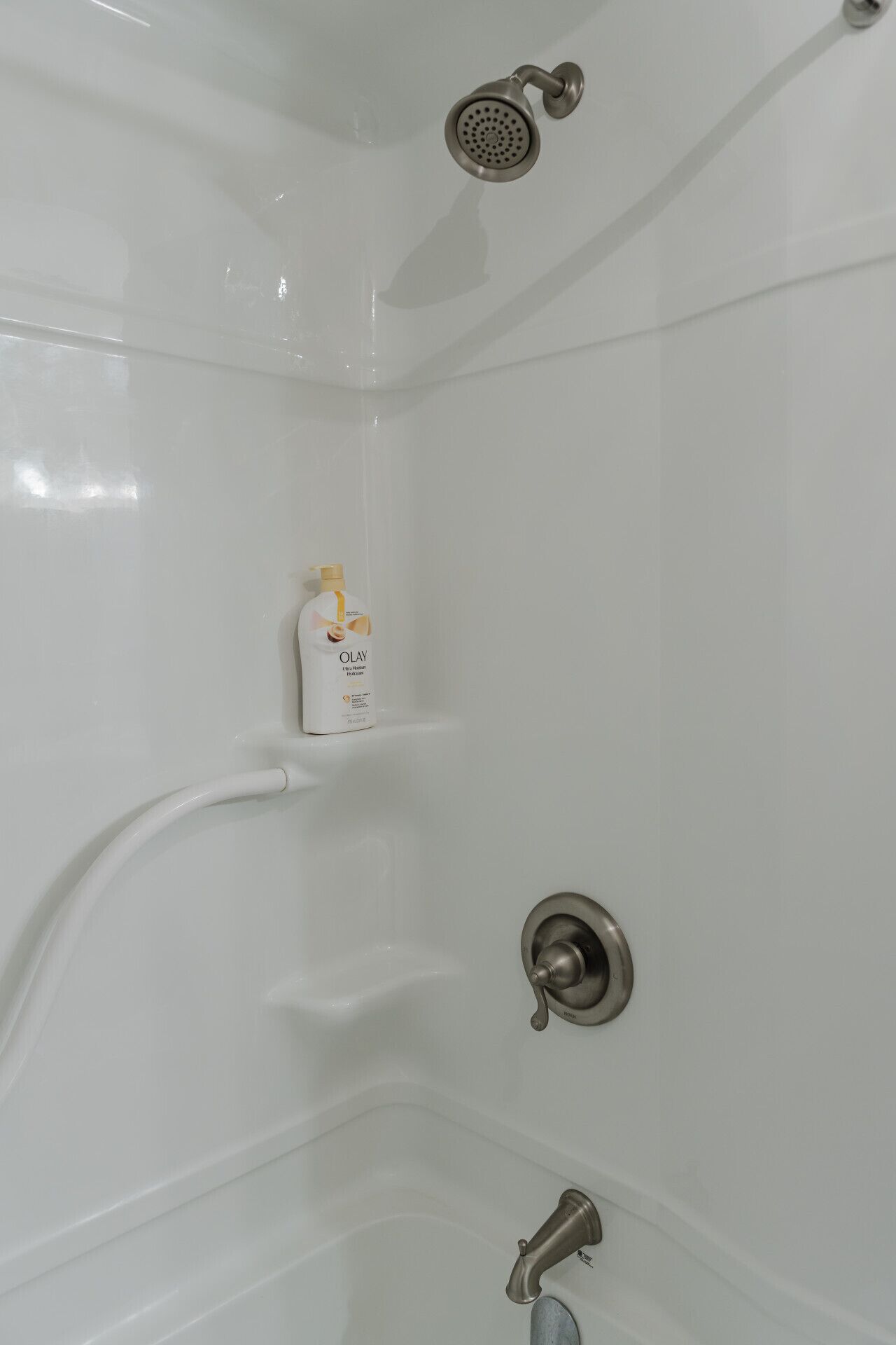 Une baignoire blanche avec un pommeau de douche à main, un flacon de lotion Olay et un robinet.