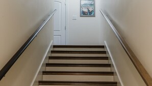 Un escalier avec des marches en bois et des rampes en métal, menant à une porte sur laquelle est accrochée une image encadrée.