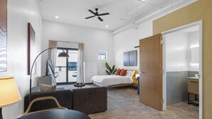 Moderni hotellihuone, jossa on sänky, työpöytä, tuoli, sohva ja parveke, jolta on näkymä.