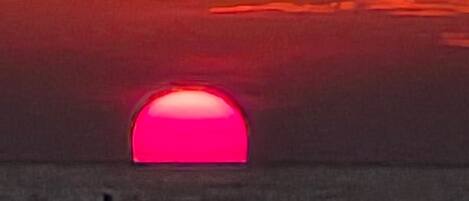 Ein Sonnenuntergang über einem Gewässer, im Vordergrund die Silhouette eines Gebäudes.