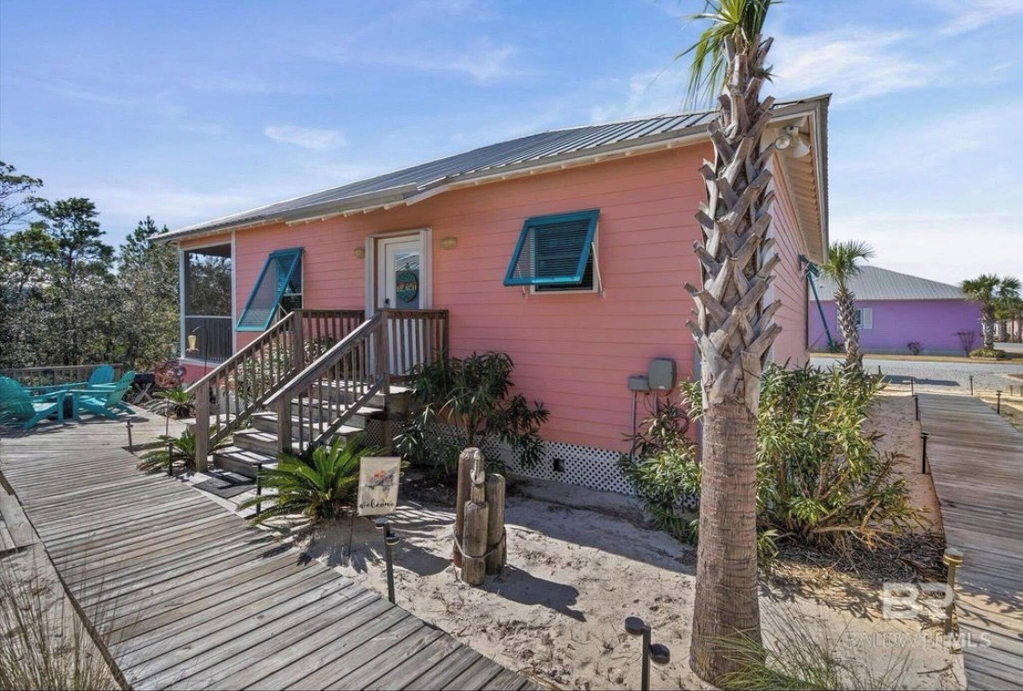 A pink house with a wooden deck, a staircase, and a small garden with plants and a cactus.