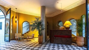 A lobby with checkered flooring, a reception desk, seating area, and large potted plants. - Suites and Spa - BY XO Riad (Marrakech)