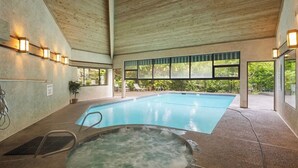 Une piscine intérieure avec un jacuzzi, entourée de fenêtres et surmontée d’un plafond en bois.