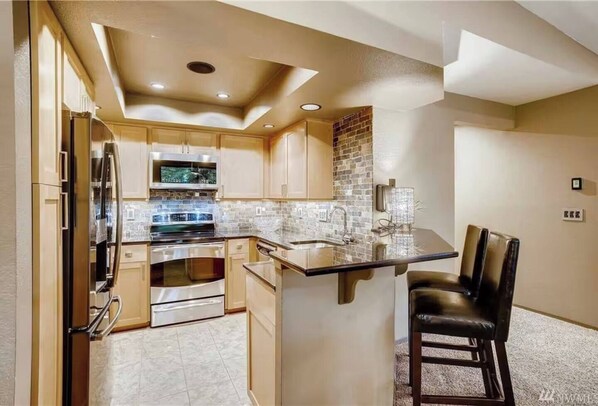 A modern kitchen with a central island, stainless steel appliances, and a brick accent wall. - Downtown Bellevue 2BR Condo Free Reserved Parking (Bellevue)