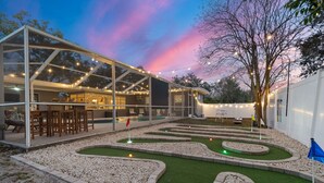 Een modern huis met een glazen patio, een kleine tuin met kronkelende paden en lichtslingers.