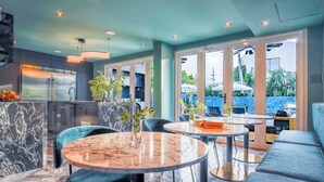 A modern kitchen with a stainless steel refrigerator, a sink, and a dining area with round tables and blue chairs. - Portofino 4BD Suite Pool Resort Vibe (San Juan)