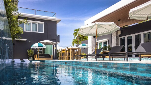 A swimming pool with lounge chairs and umbrellas, surrounded by modern buildings with large windows and a clear sky. - Portofino 4BD Suite Pool Resort Vibe (San Juan)