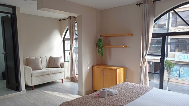 A hotel room with a bed, a sofa, a wooden cabinet, and a large window with a view of the outside. - Hostal Tayupanda (Quito)
