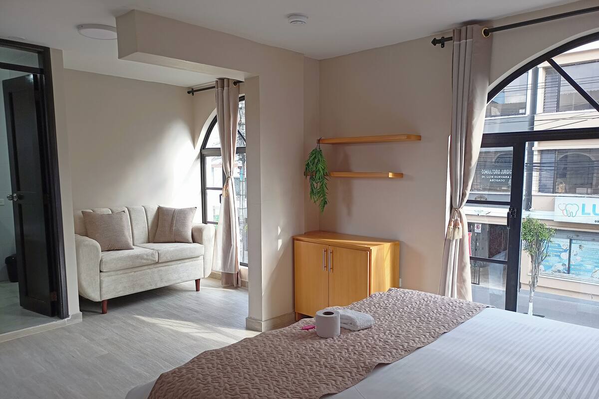 Een hotelkamer met een bed, een bank, een houten kast en een groot raam met uitzicht.