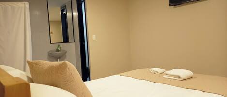 Una habitación de hotel con cama, mesita de noche, espejo, lavamanos y televisor.