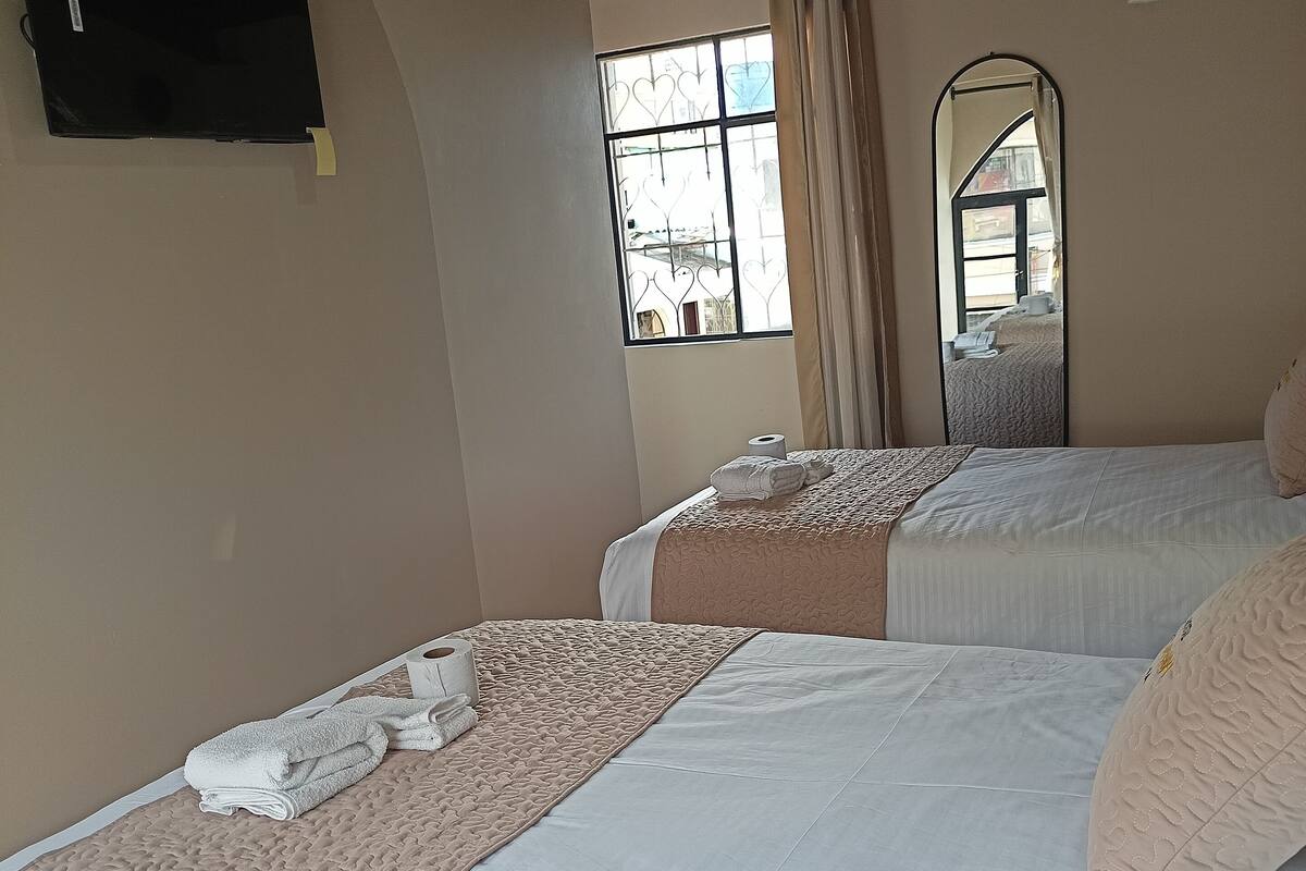 Een hotelkamer met twee bedden, een raam met gordijnen, een spiegel en een aan de muur bevestigde televisie.