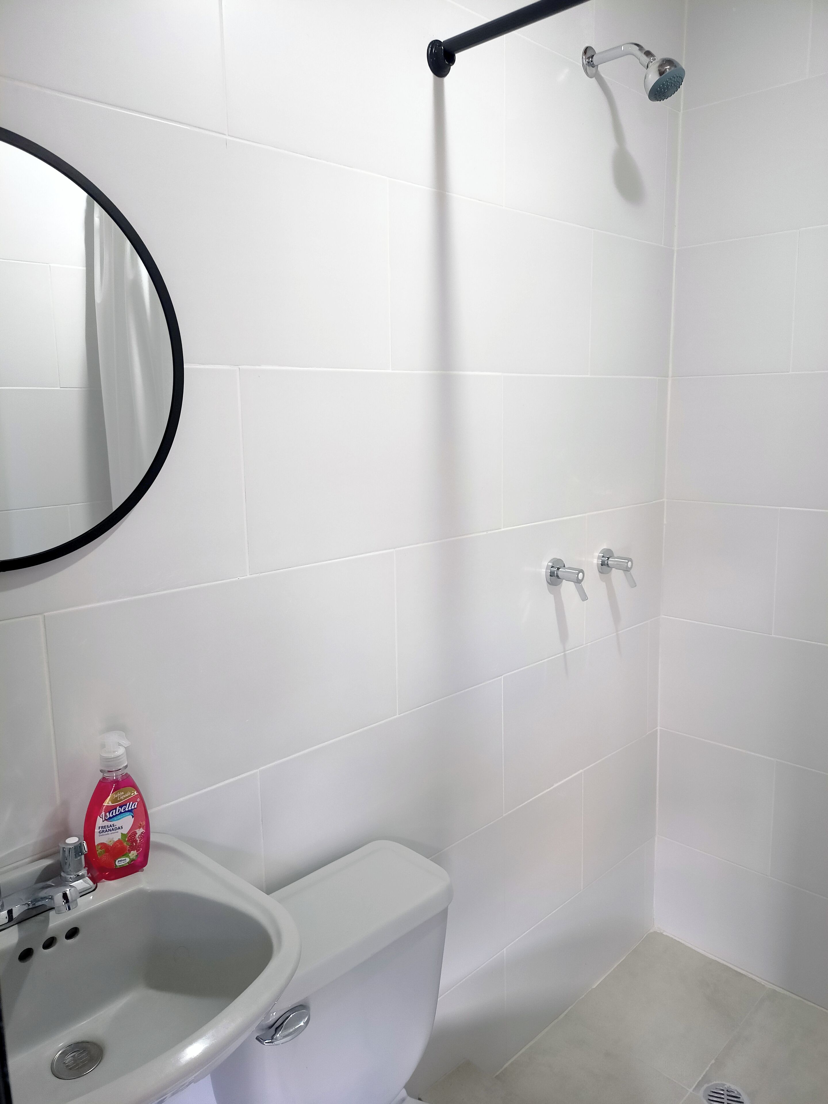 A bathroom with white tiles, a toilet, a sink, a mirror, and a shower.